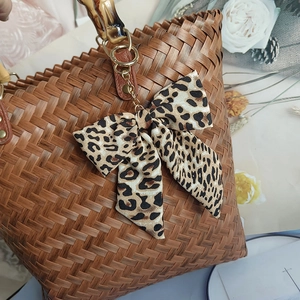 Woven handbag with leopard print bow and bamboo handle displayed with dried flowers