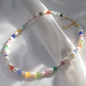 Macro shot of colorful beads and baroque pearls necklace with a star pendant on white silk