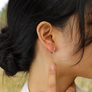 Minimalist silver stainless steel hoop earrings worn by a model in natural sunlight