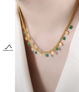 Detail of a gold stainless steel necklace featuring small gold and green star charms