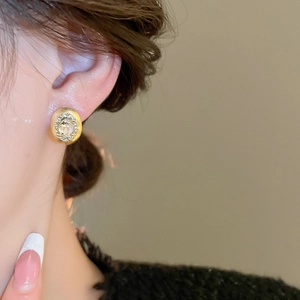 Close-up of a gold oval earring with cubic zirconia inlay worn by a model in warm light