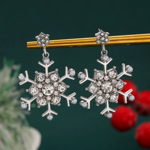 Detailed close-up of sparkling snowflake earrings with pearls and crystals on a green background