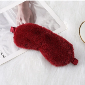 Close-up of soft red plush sleep mask with elastic strap on white faux fur background