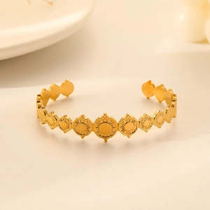 Detail of gold open bangle with embossed sun pattern charms on a soft beige background