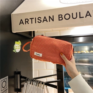 Détail d'une trousse à maquillage en toile à carreaux orange avec fermeture éclair et étiquette