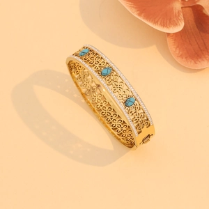 Detailed view of a gold hollow-out bangle set with turquoise stones and cubic zirconia