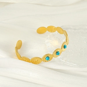 Gold plated open turquoise bangle with embossed sun pattern on white silk background