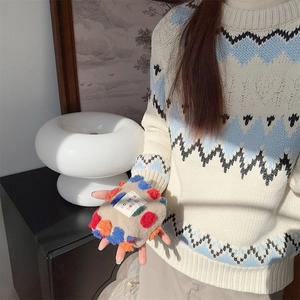 Dettaglio della trousse in peluche retrò con pompon colorati tenuta in mano