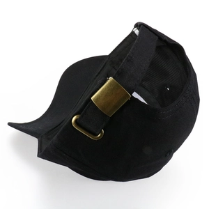 Detail view of the bronze metal adjustable buckle on the back of the black cotton baseball cap