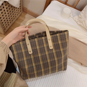 Detail of plaid tote bag featuring brown check pattern and leather handles with rivets