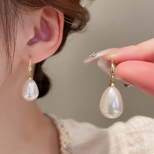 Close-up of elegant gold hook earring featuring a large white teardrop pearl on an ear