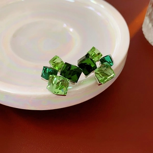 Macro shot of green faceted crystal stud earrings on white ceramic and red background