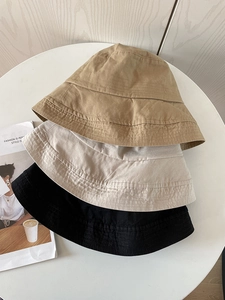 Close-up of three cotton bucket hats in khaki, beige, and black on a white tray