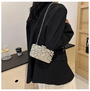 Detalle de bolso de fiesta plateado con textura fluida y fina correa de cadena metálica