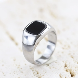 Macro shot of silver polished signet ring with a square black stone on a stone base