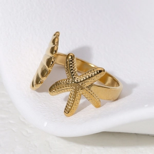 Goldener Edelstahlring mit Seestern und Muschel auf weißer strukturierter Oberfläche