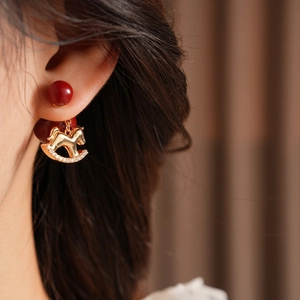 Detailed view of gold rocking horse earring with red bead and sparkling zircon inlay