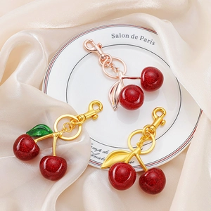 Charming red glitter cherry keychain with gold and rose gold hardware on silk background