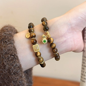 Detailed view of beaded tiger eye bracelets with golden hollow charm on a wrist