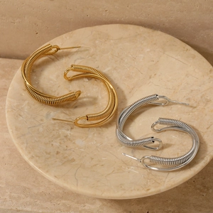 Double-layered twisted C-shaped earrings in gold and silver finish on marble tray
