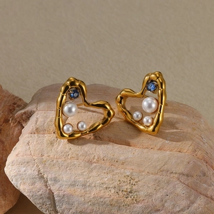 Detailed shot of golden heart earrings with pearls and a blue gemstone on stone