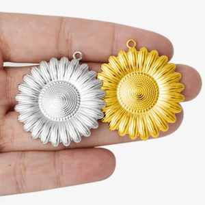 Hand holding vintage sunflower pendants in gold and silver finish for DIY jewelry