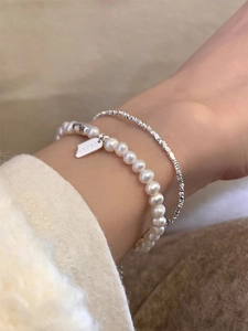 Close-up of stacked s925 silver lucky charm bracelet and white freshwater pearl strand