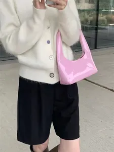 Detailed view of pink patent leather crescent shoulder bag held by a model outdoors