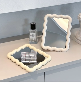 Close-up of wavy cream-colored frames on desk-standing makeup mirrors in a lifestyle setting