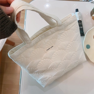 Detail of white quilted tote bag featuring shell-pattern embroidery and a simple wish label