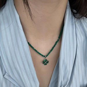 Detail of green beaded clover necklace with crystal pendant on a female model