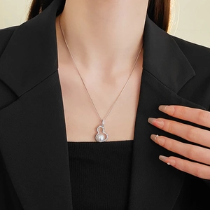 Close-up of a silver gourd-shaped pendant with a white pearl on a model's neckline