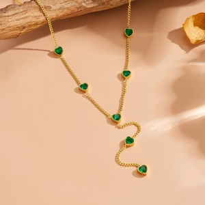 Elegant gold-plated Y-necklace featuring green heart-shaped gemstones on a wooden branch