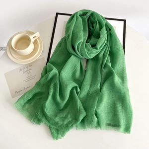 Detail of green cotton linen scarf with frayed edges and breathable texture on white table