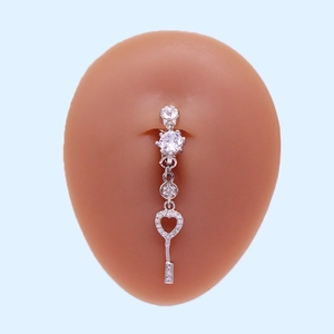 Detail of silver heart and key navel ring with crystals on a silicone belly model