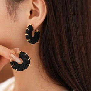 Macro detail of C-shaped black woven earrings with elegant gold bead embellishments