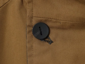 Detailed close-up of brown twill fabric with black round button and fine stitching