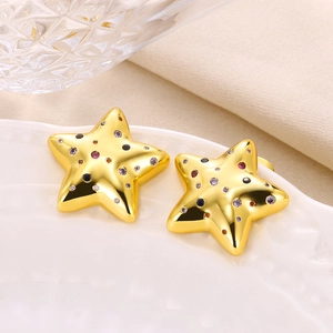 Close-up of gold star earrings with colorful zircon stones on a white ceramic plate
