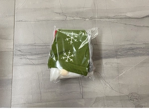 Detail of green knitted Christmas wine bag with white snowflake embroidery in clear packaging