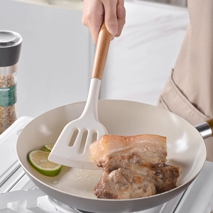Silicone slotted turner with wooden handle used for frying meat in a non-stick pan