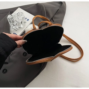 Detailansicht einer braunen Herz-Tasche mit Reißverschluss und weißem Plüsch-Anhänger