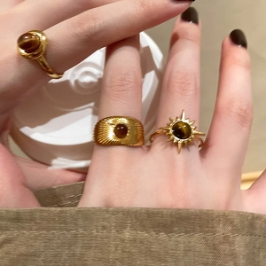 Close-up of three gold-plated oval rings with tiger eye stones worn on fingers