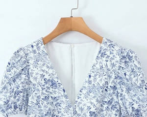 Detail of floral V-neck dress with puff sleeves on a wooden hanger with blue patterns