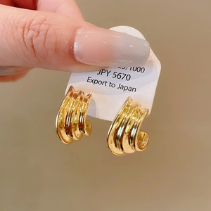 Detailed close-up of golden geometric spiral earrings with textured multi-layered waves