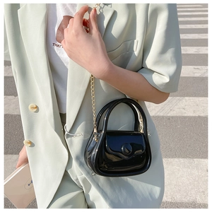 Mini black glossy chain bag with golden strap shown in a fashionable street style view