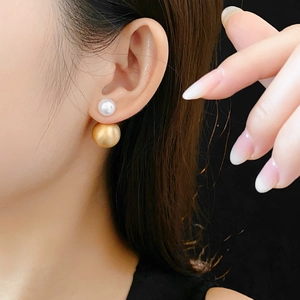 Close-up of double-bead earrings with white pearl and golden brushed metal sphere