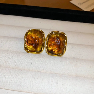 Detailed macro view of vintage gold-rimmed amber resin earrings on a velvet tray
