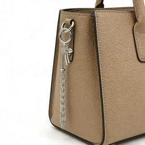Dettaglio di un ciondolo a fiocco d'argento su una borsa in pelle beige con grana litchi