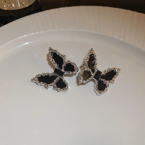 Detail shot of silver butterfly stud earrings with black enamel on a textured plate