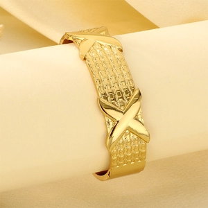 Detailed macro of a gold-plated woven texture bangle featuring polished cross X elements